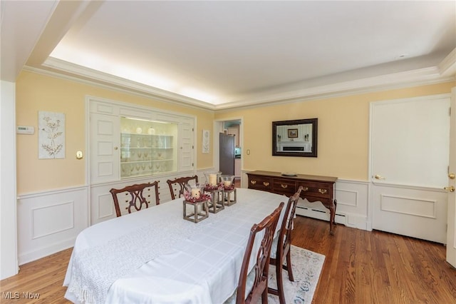 dining room featuring a wainscoted wall, a baseboard radiator, and a decorative wall