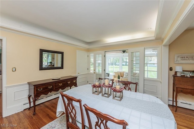 dining space with crown molding, a baseboard heating unit, wood finished floors, and a wainscoted wall