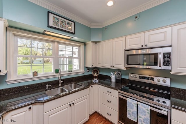 kitchen with ornamental molding, white cabinets, a sink, dark stone countertops, and stainless steel appliances