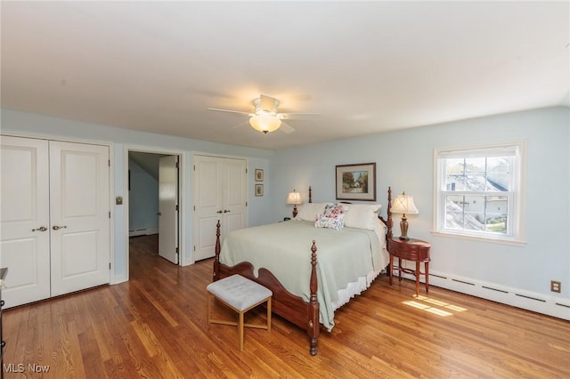 bedroom featuring a ceiling fan, multiple closets, baseboard heating, and wood finished floors