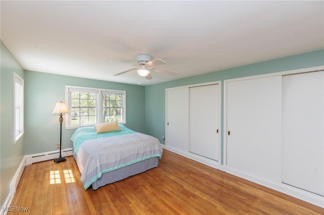 bedroom featuring wood finished floors, baseboards, multiple closets, and a baseboard heating unit