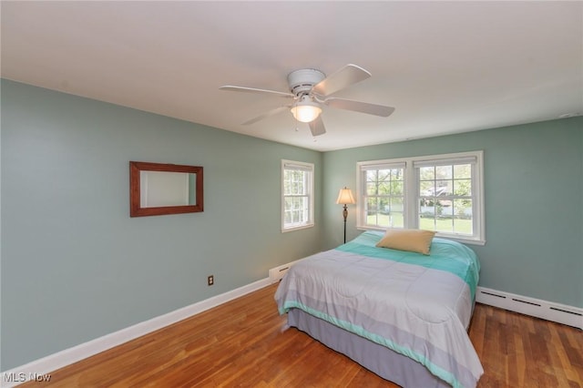 bedroom featuring a ceiling fan, baseboards, a baseboard heating unit, and wood finished floors