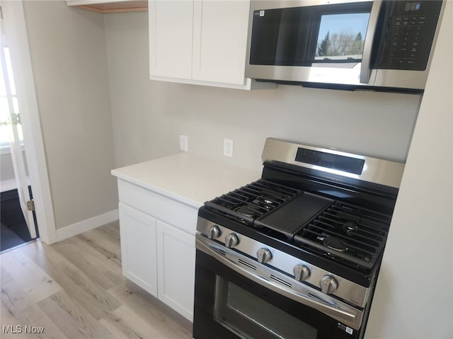 kitchen with appliances with stainless steel finishes, light countertops, baseboards, white cabinets, and light wood-style flooring