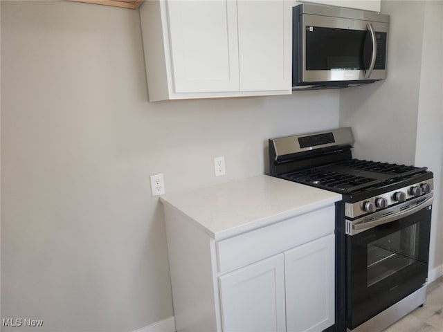 kitchen with baseboards, light stone countertops, stainless steel appliances, and white cabinetry