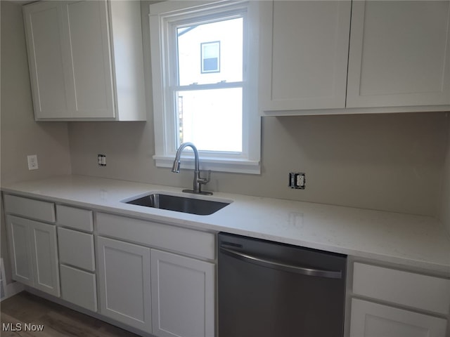 kitchen with stainless steel dishwasher, white cabinetry, light stone countertops, and a sink