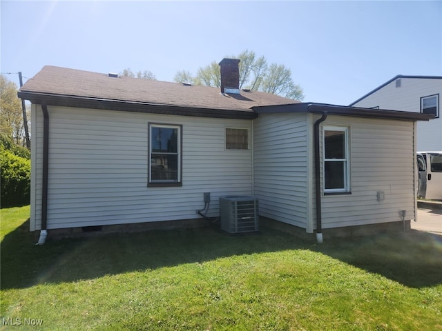 rear view of property with a lawn, central air condition unit, and a chimney