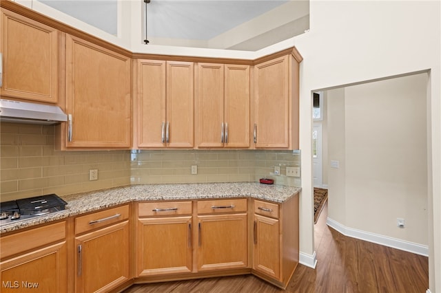 kitchen with wood finished floors, light stone countertops, under cabinet range hood, backsplash, and stainless steel gas stovetop