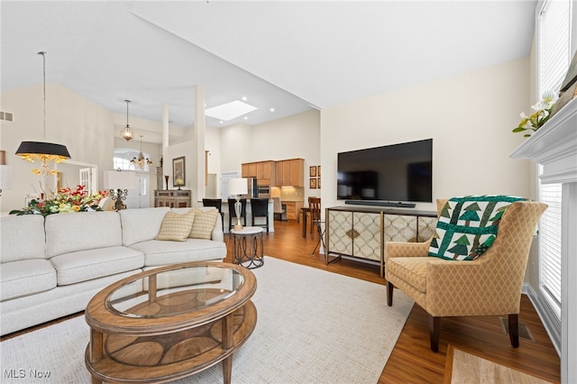 living area featuring high vaulted ceiling, a notable chandelier, wood finished floors, and visible vents