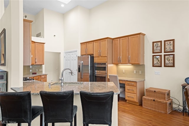 kitchen featuring tasteful backsplash, a sink, light wood finished floors, a peninsula, and stainless steel appliances