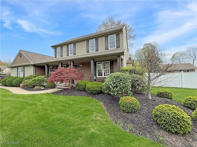 traditional home featuring a porch, a front lawn, and fence