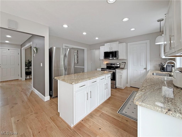 kitchen featuring a kitchen island, white cabinets, a sink, light wood finished floors, and appliances with stainless steel finishes