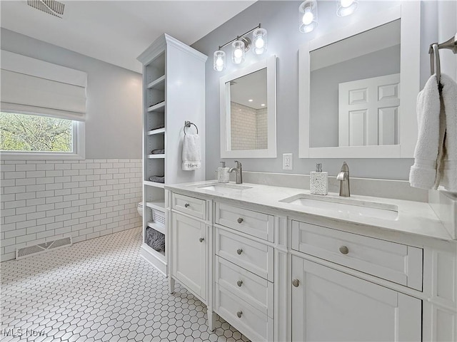 full bathroom featuring a sink, a wainscoted wall, double vanity, and visible vents