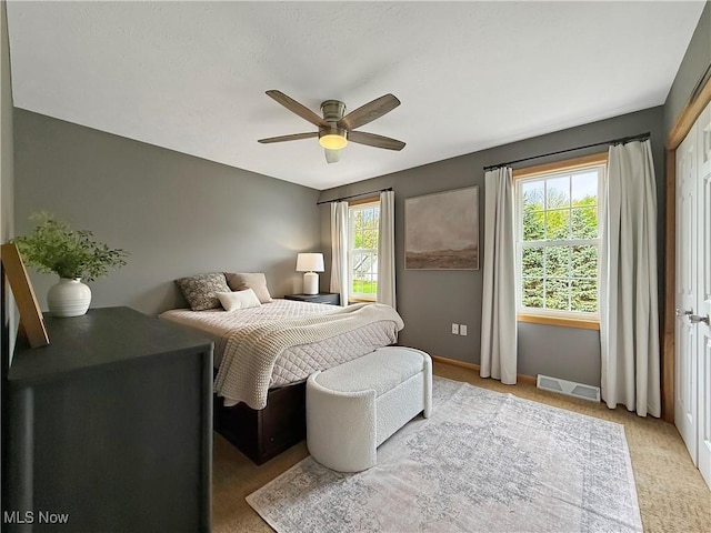 bedroom with visible vents, a ceiling fan, baseboards, and light colored carpet