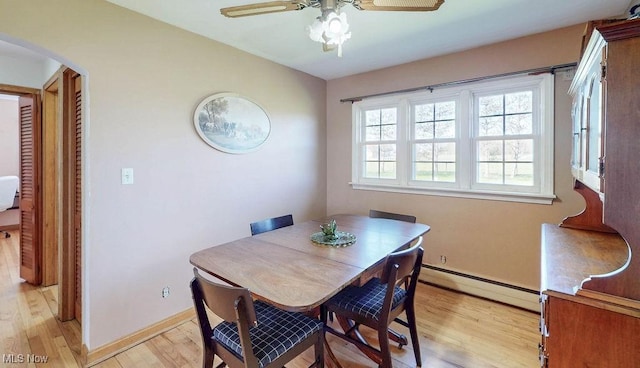 dining space featuring a ceiling fan, arched walkways, light wood-type flooring, baseboards, and a baseboard heating unit