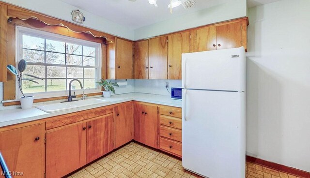 kitchen with freestanding refrigerator, brick patterned floor, light countertops, brown cabinets, and a sink