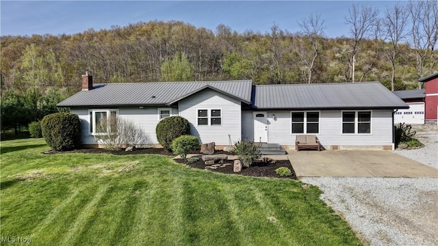 single story home with metal roof, driveway, a front lawn, and a forest view