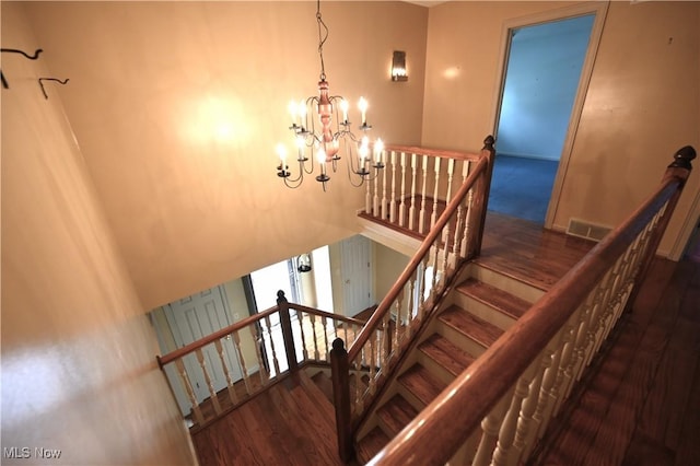 staircase with an inviting chandelier, wood finished floors, and visible vents