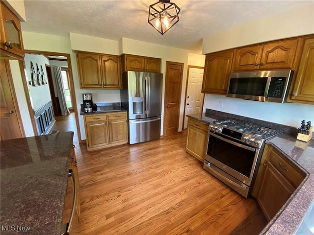 kitchen featuring light wood-style floors, dark stone countertops, appliances with stainless steel finishes, and brown cabinets