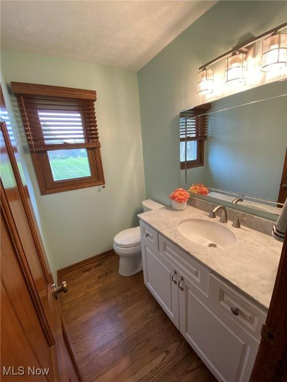 bathroom with vanity, wood finished floors, toilet, baseboards, and a textured ceiling