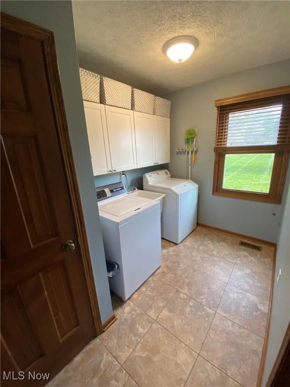 laundry room featuring a textured ceiling, cabinet space, light tile patterned floors, baseboards, and washer and clothes dryer