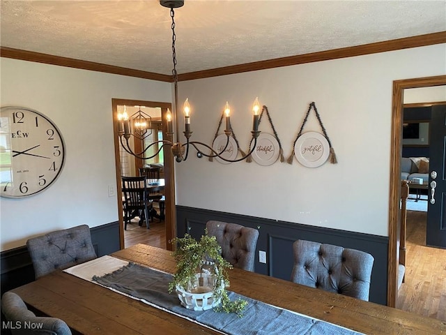 dining area featuring a textured ceiling, wainscoting, wood finished floors, and a chandelier