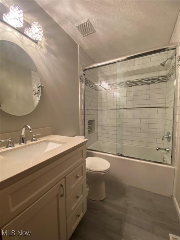 full bath with shower / bath combination with glass door, vanity, toilet, a textured ceiling, and visible vents