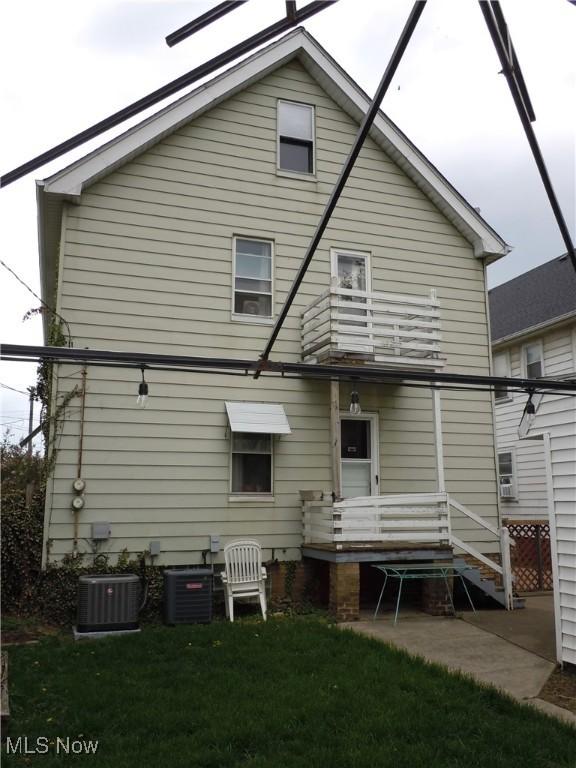 rear view of house with central AC unit, a yard, and a balcony