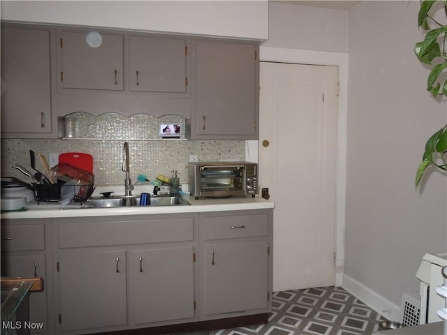 kitchen featuring a sink, light countertops, gray cabinets, decorative backsplash, and a toaster