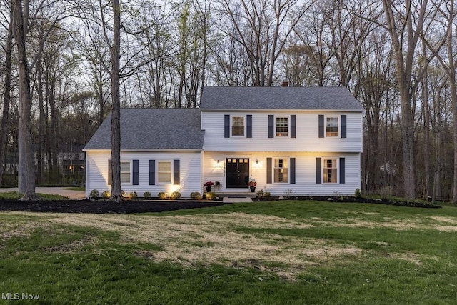 colonial home with a shingled roof and a front yard