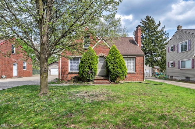 view of front facade featuring brick siding, a chimney, a front yard, and a detached garage