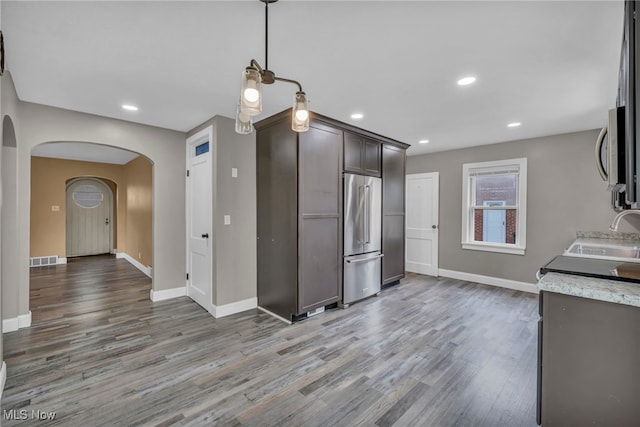 kitchen featuring wood finished floors, baseboards, arched walkways, a sink, and stainless steel appliances