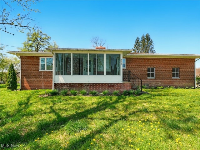 rear view of house featuring a sunroom, a lawn, and brick siding