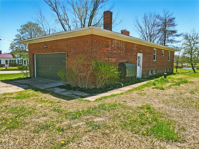view of side of property featuring brick siding, driveway, a chimney, and heating fuel