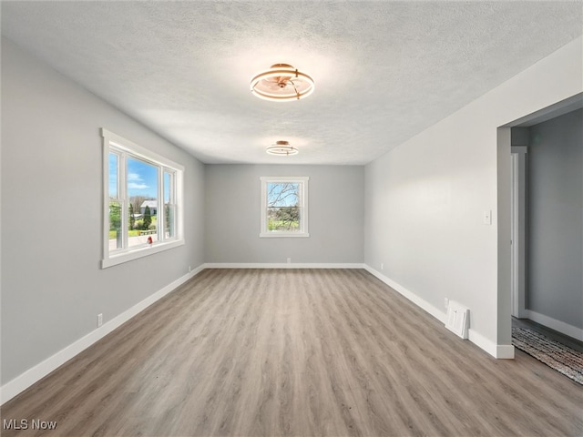 unfurnished room featuring baseboards, a textured ceiling, visible vents, and wood finished floors