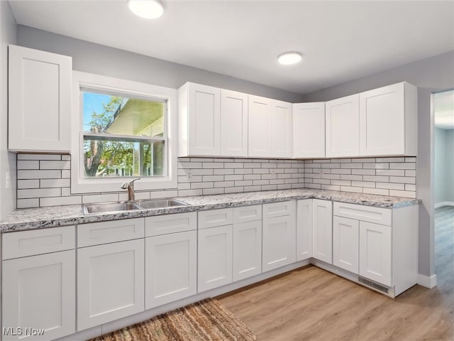 kitchen featuring tasteful backsplash, light stone countertops, a sink, white cabinets, and light wood finished floors
