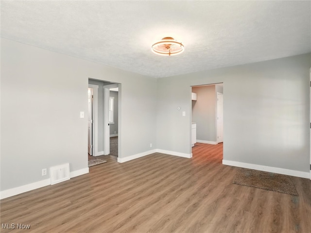 unfurnished room with baseboards, a textured ceiling, wood finished floors, and visible vents