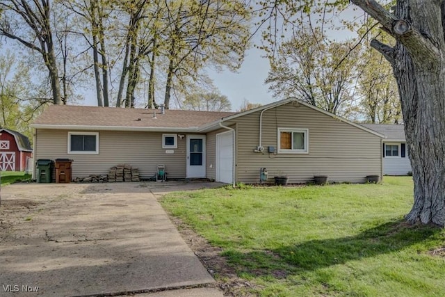 rear view of property featuring a lawn, an attached garage, concrete driveway, and a storage unit