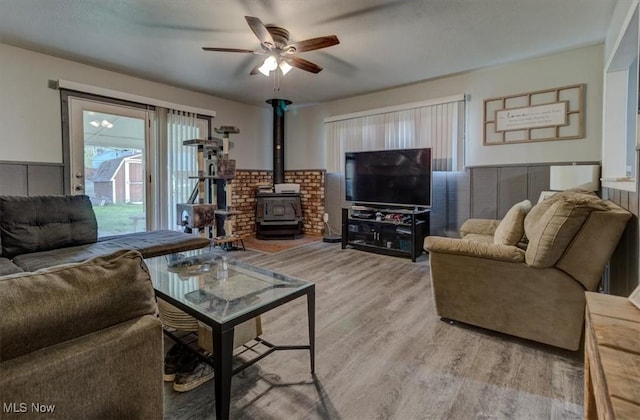 living room with ceiling fan, a wood stove, and wood finished floors