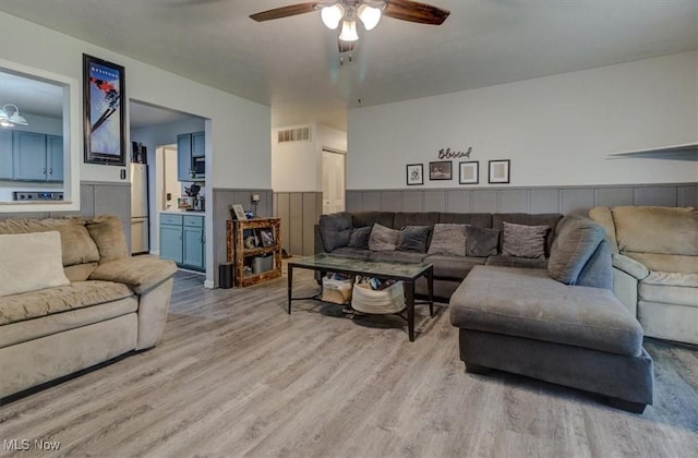 living area featuring visible vents, a ceiling fan, wainscoting, and light wood finished floors