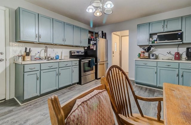 kitchen with a notable chandelier, a sink, light wood finished floors, light countertops, and stainless steel appliances