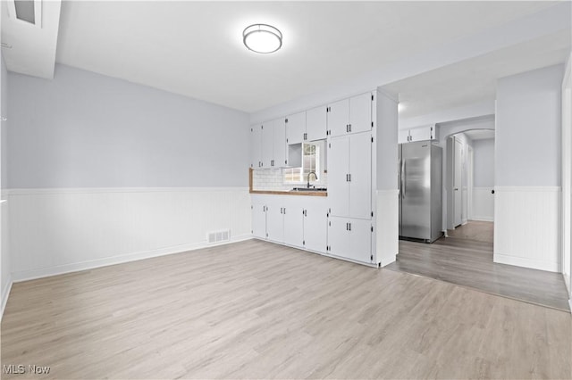 unfurnished living room featuring visible vents, wainscoting, a sink, and light wood-type flooring