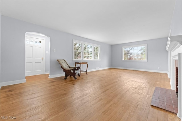 living area with arched walkways, baseboards, and light wood finished floors