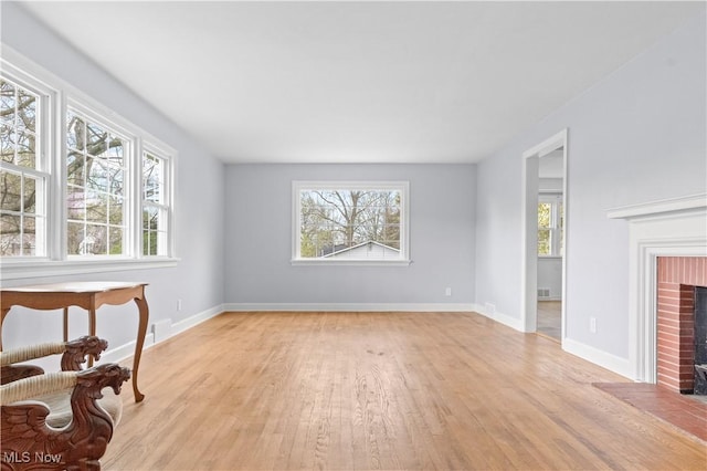 unfurnished living room featuring a brick fireplace, baseboards, visible vents, and light wood finished floors