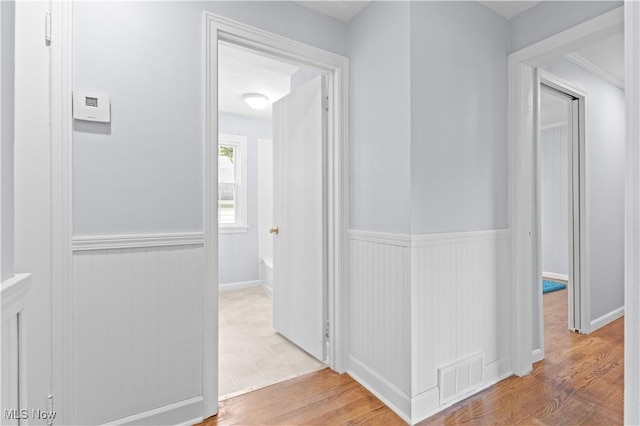 corridor with visible vents, wood finished floors, and a wainscoted wall
