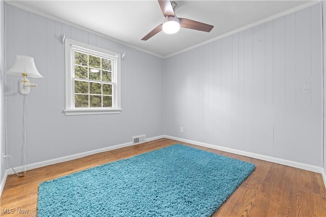 spare room with a ceiling fan, visible vents, crown molding, wood finished floors, and baseboards