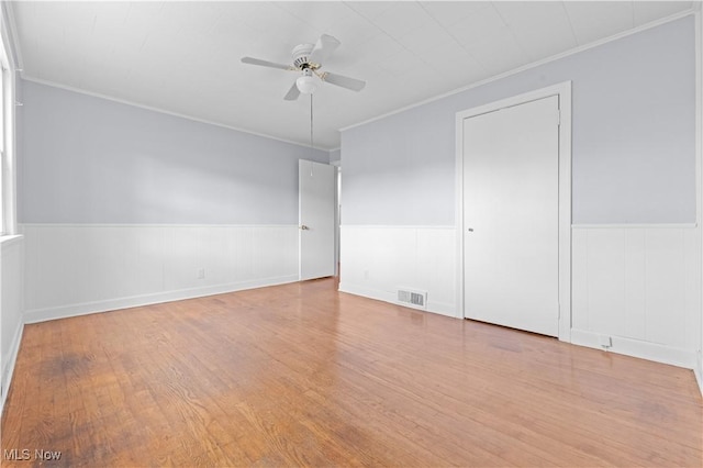 spare room featuring ornamental molding, visible vents, wainscoting, and wood finished floors