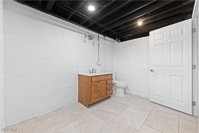 bathroom with concrete block wall, vanity, and toilet