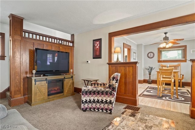 living area with crown molding, baseboards, ceiling fan, and a glass covered fireplace