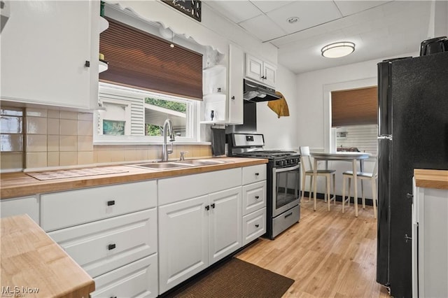 kitchen featuring wooden counters, stainless steel range with gas stovetop, a sink, freestanding refrigerator, and under cabinet range hood