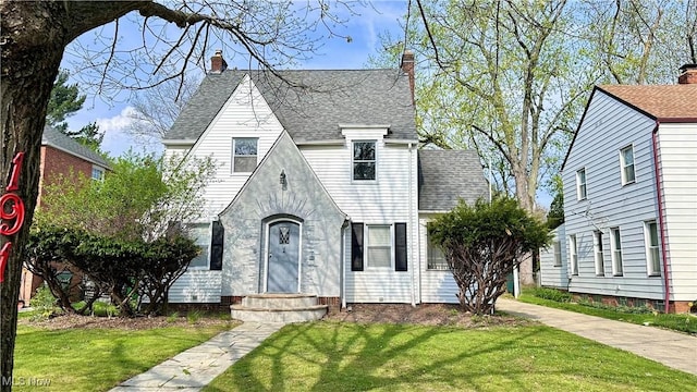 tudor home with a chimney, a shingled roof, and a front yard